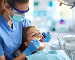 Girl with brown hair undergoing dental exam by woman in blue scrubs