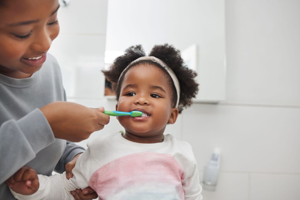 Woman brushing little girl's teeth with a green and blue toothbrush